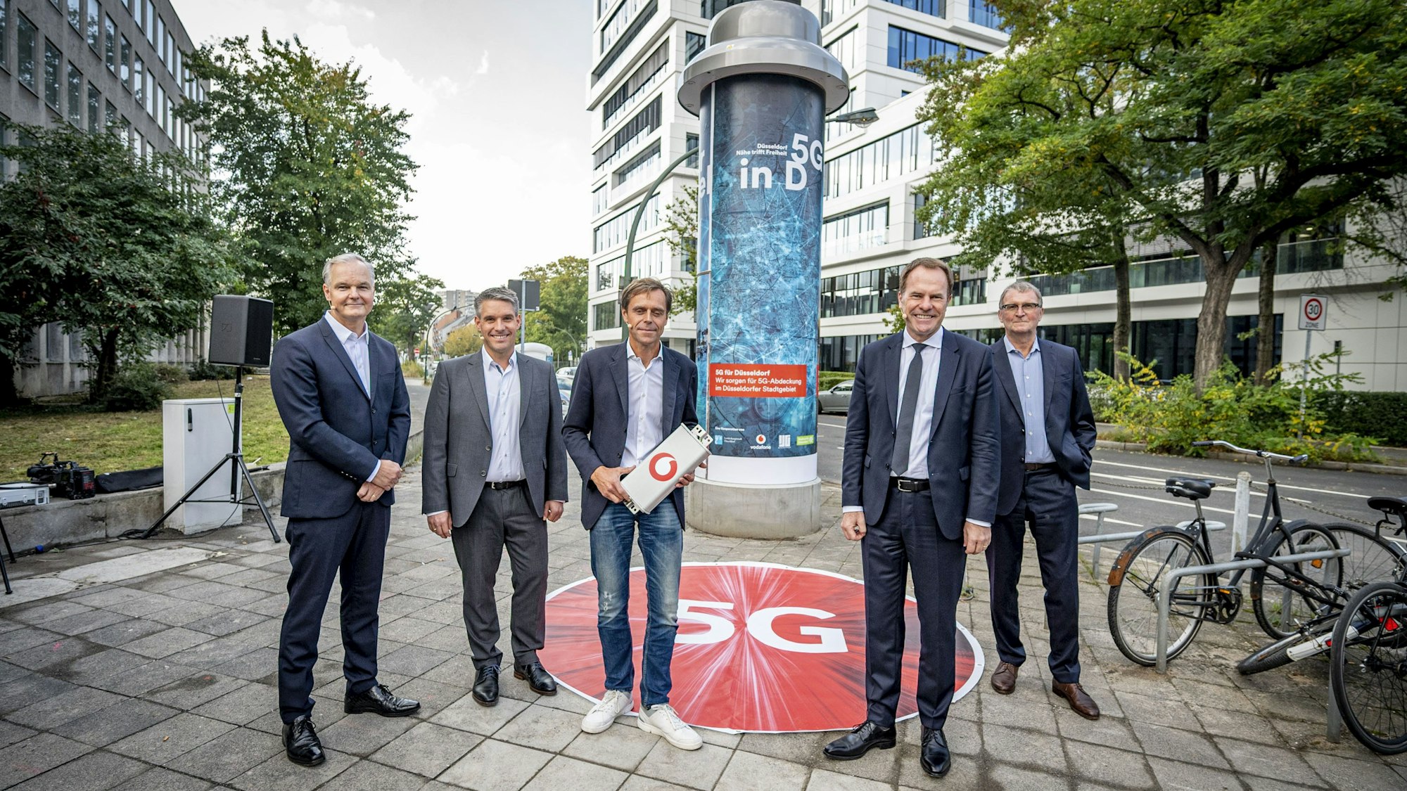 Alle Beteiligten stehen vor einer Litfaßsäule in Düsseldorf.