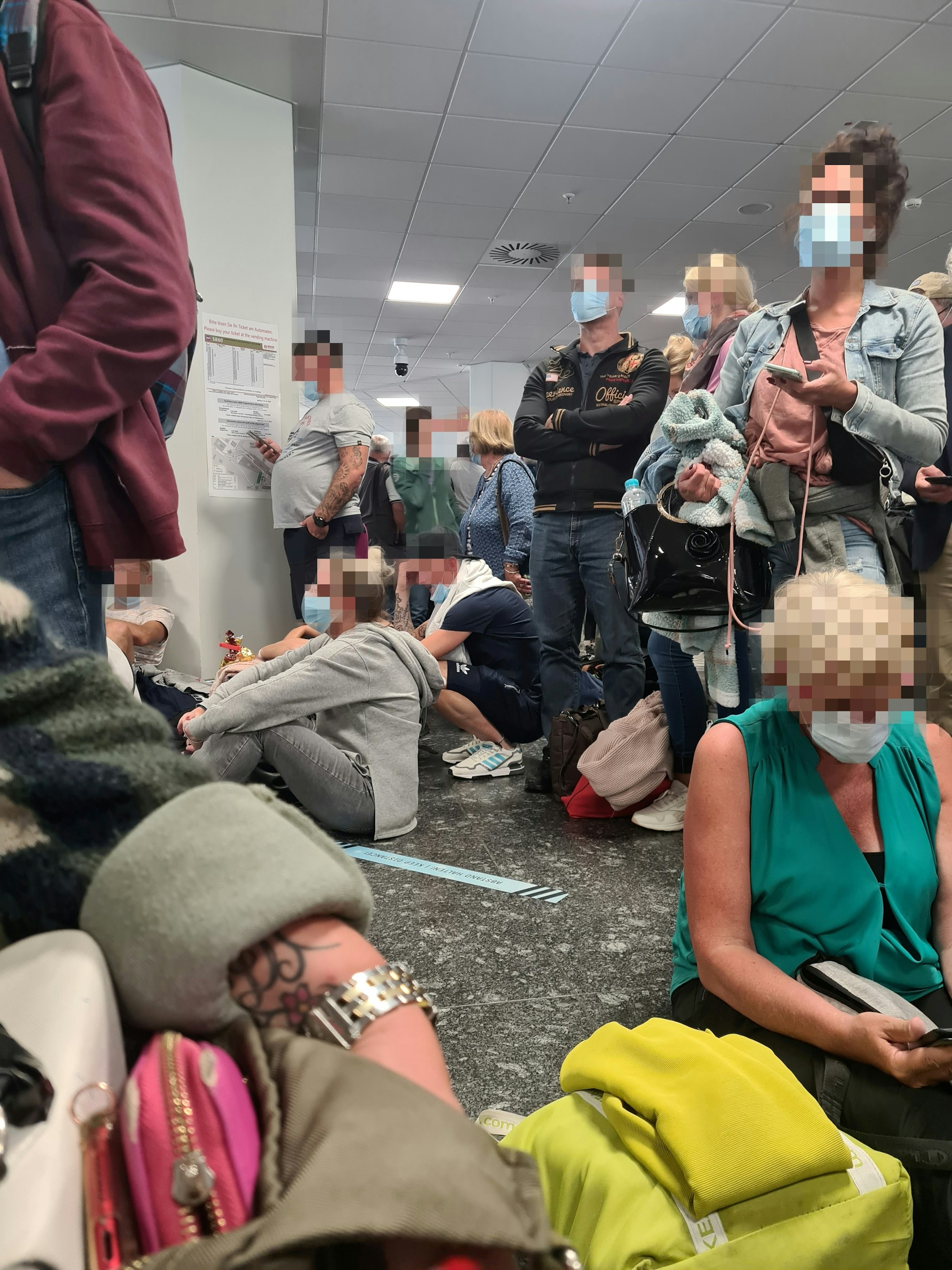 Reisende sitzen auf dem Boden an der Gepäckausgabe und warten.