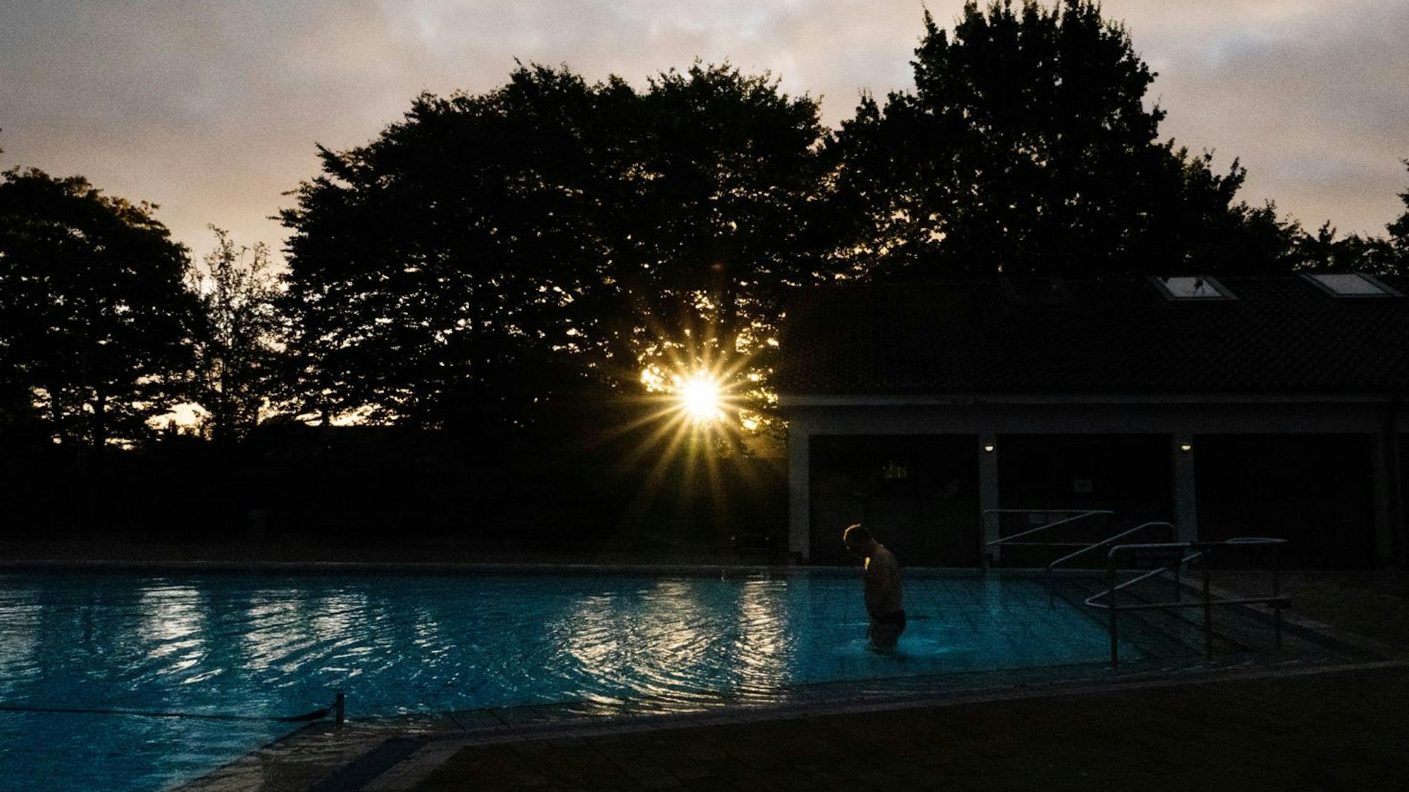 Großburgwedel: Ein Badegast steigt am frühen Morgen bei Sonnenaufgang ins Schwimmbecken im Freibad Großburgwedel in der Region Hannover.