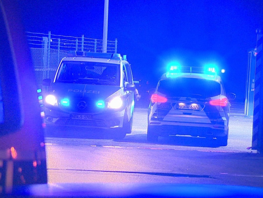 Polizisten passieren in Polizeifahrzeugen ein Tor am Flughafen Weeze, wo ein Auto einen Zaun an einer Rollbahn durchbrochen hat.