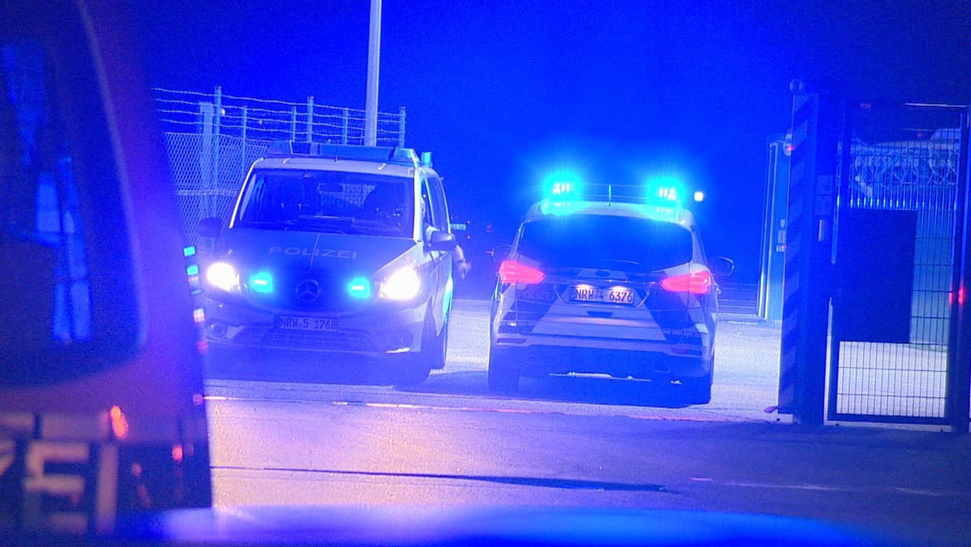 Polizisten passieren in Polizeifahrzeugen ein Tor am Flughafen Weeze, wo ein Auto einen Zaun an einer Rollbahn durchbrochen hat.