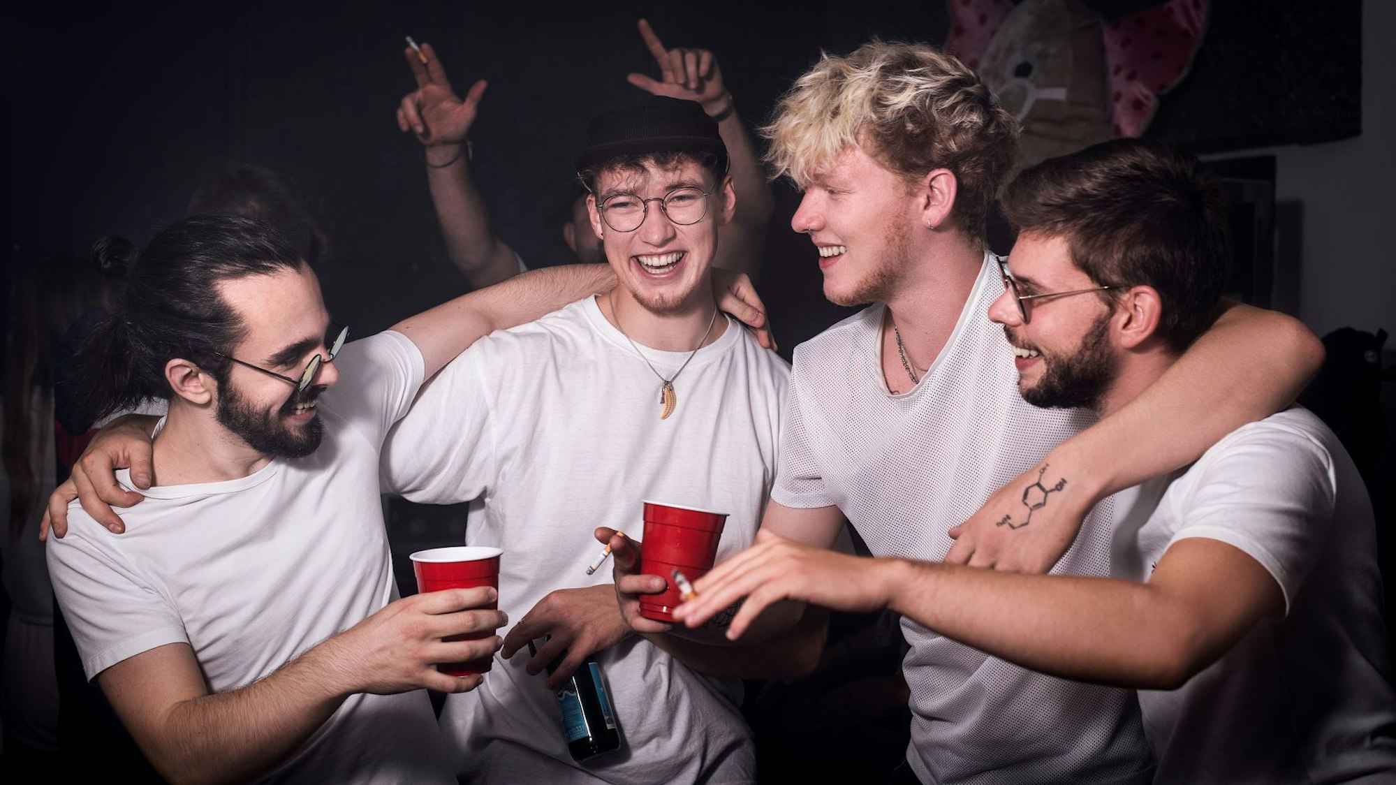 Band King Loui feiert Arm in Arm, mit Bechern und Zigaretten in den Händen.