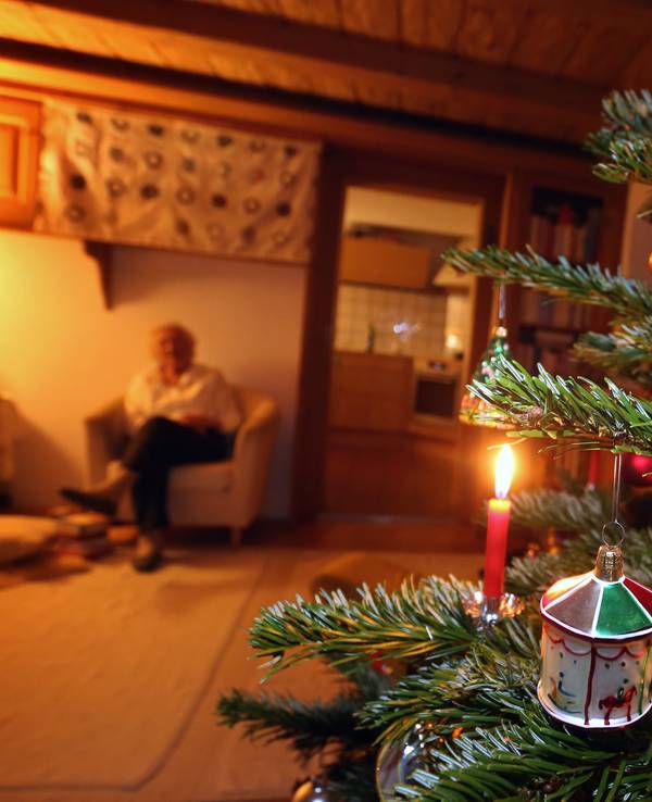 Auf dem Foto sieht man im rechten Teil des Bildes einen geschmückten Tannenbaum, im Hintergrund sitzt eine ältere Frau.