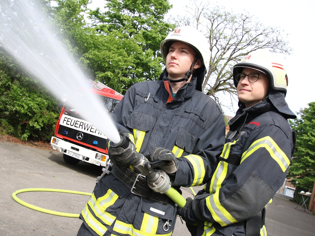 Zwei Feuerwehrmänner halten einen Löschschlauch.