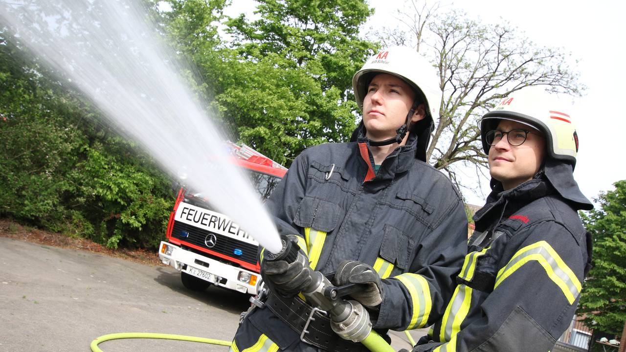 Zwei Feuerwehrmänner halten einen Löschschlauch.