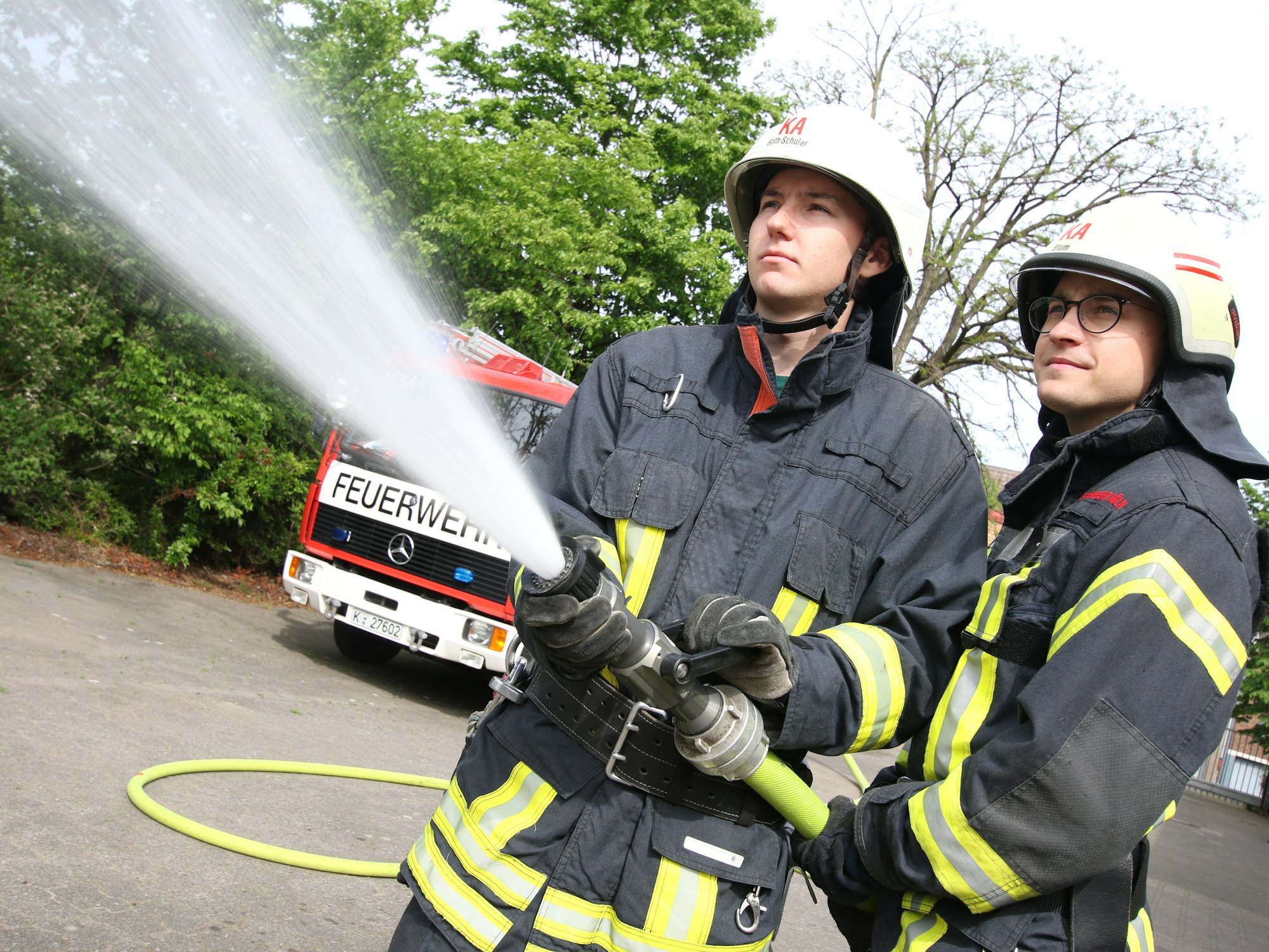 Zwei Feuerwehrmänner halten einen Löschschlauch.