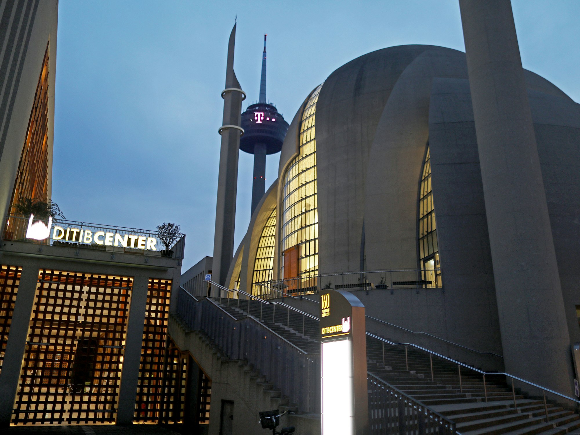 Die Moschee in Köln-Ehrenfeld ist am Morgen beleuchtet, dahinter ist der Kölner Fernsehturm zu sehen.