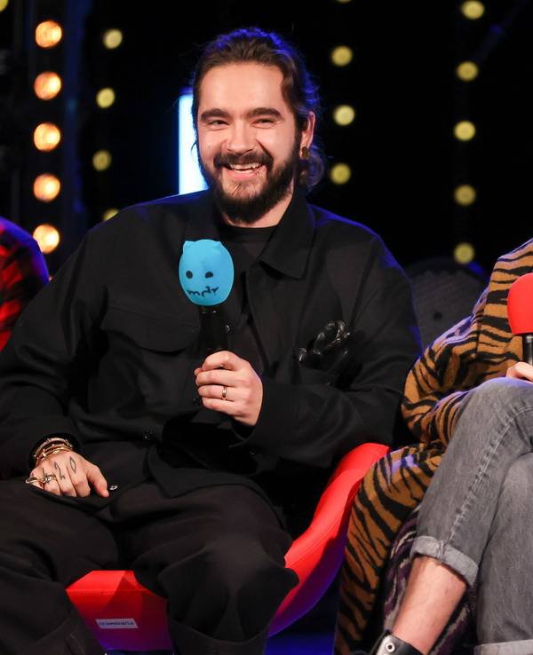 Tom und Bill Kaulitz von der Band Tokio Hotel sitzen während einer Radioshow auf einer Bühne mit jeweils einem Mikrofon in der Hand.