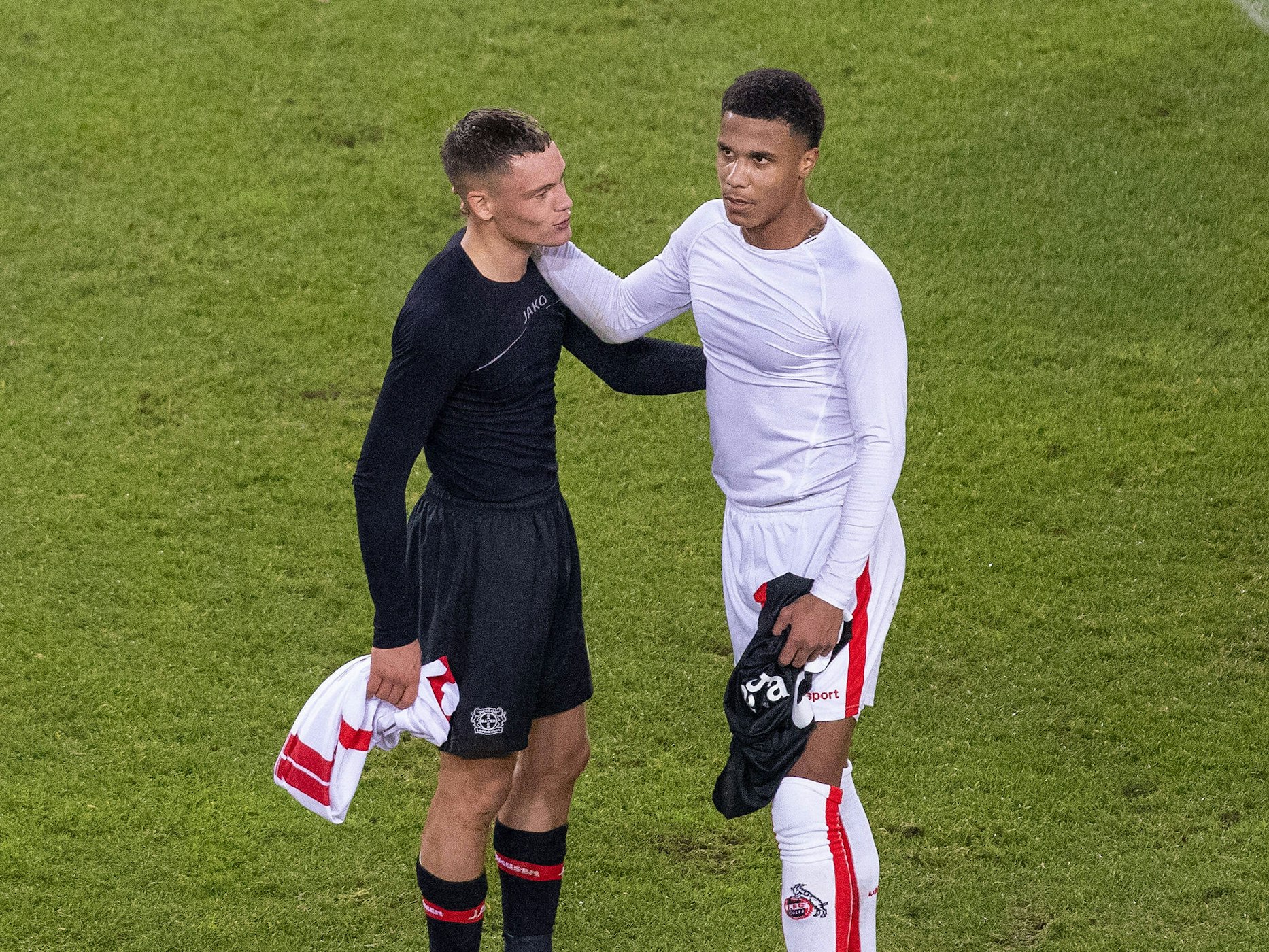 Florian Wirtz und Ismail Jakobs unterhalten sich nach Spielende, beide legen die Arme umeinander.