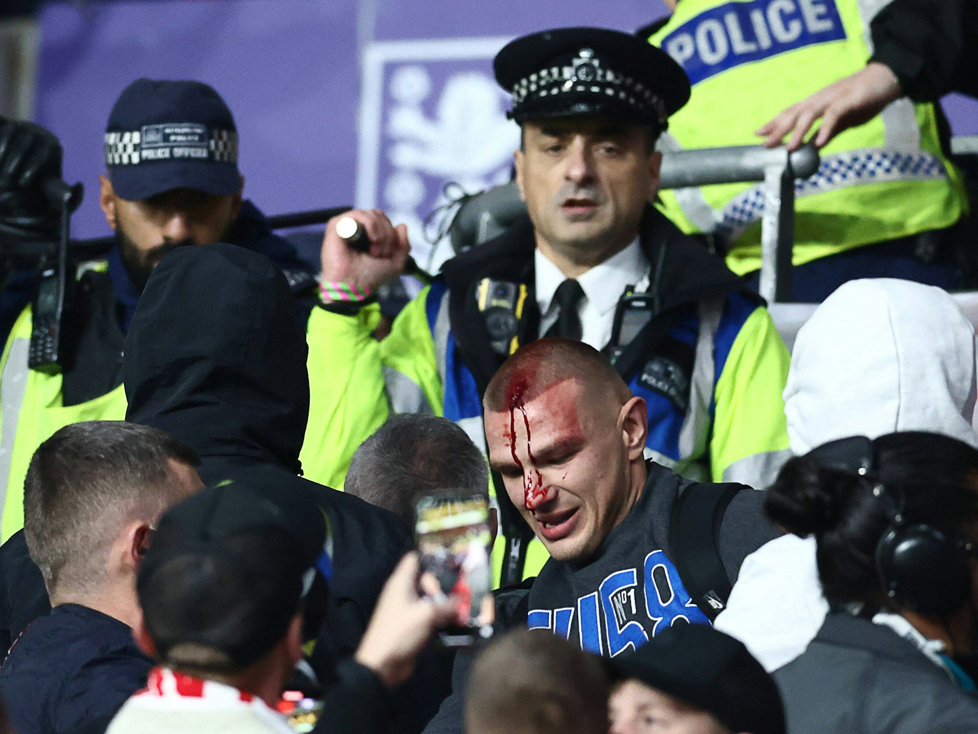Ein Polizist hat seinen Schlagstock erhoben, vor ein Ungar, der am Kopf blutet.