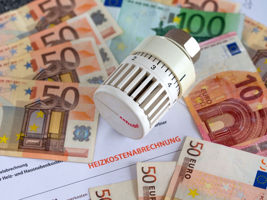 Ein Heizungsthermostat liegt auf der Heizkostenabrechnung und Euro-Geldscheinen.