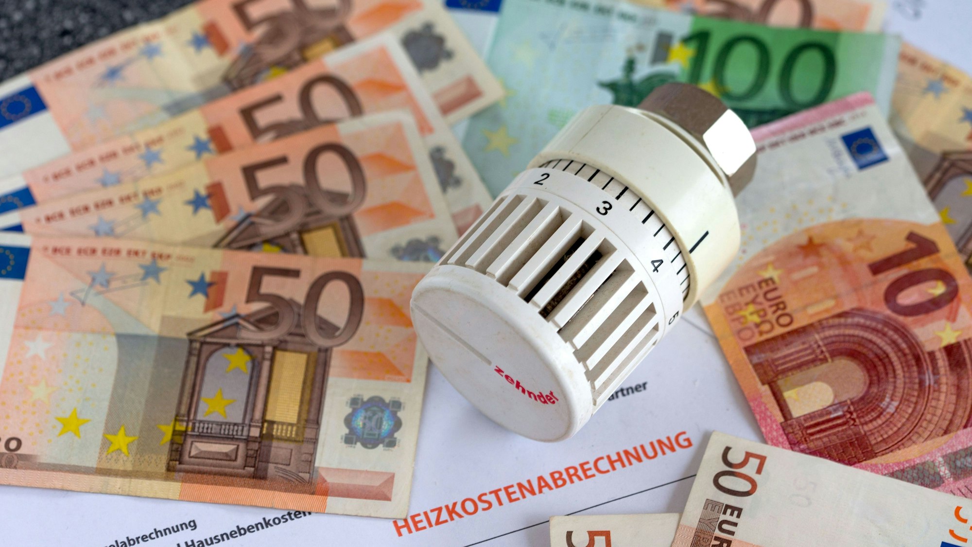 Ein Heizungsthermostat liegt aauf der Heizkostenabrechnung und Euro-Geldscheinen.