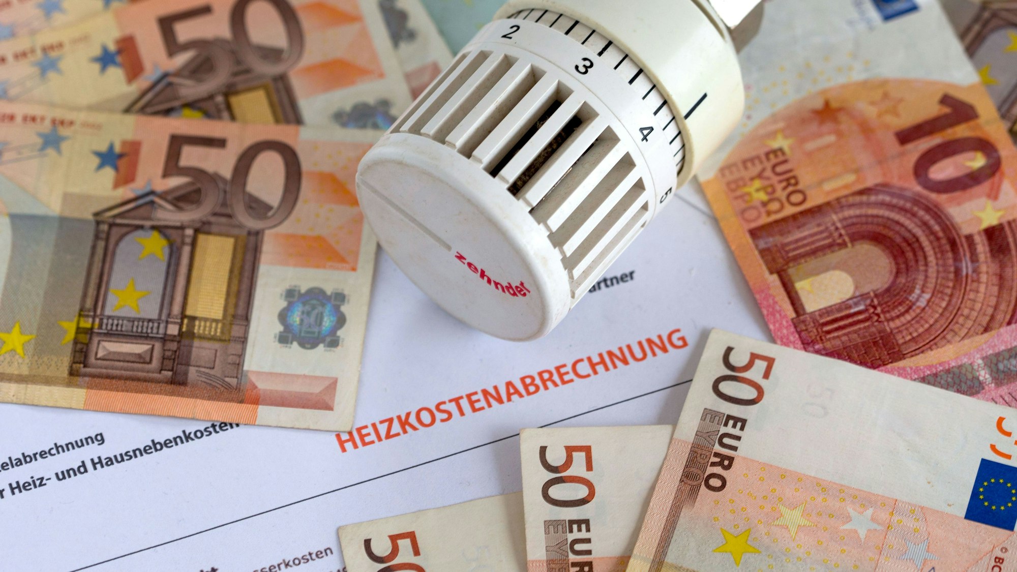 Ein Heizungsthermostat liegt auf der Heizkostenabrechnung und Euro-Geldscheinen.