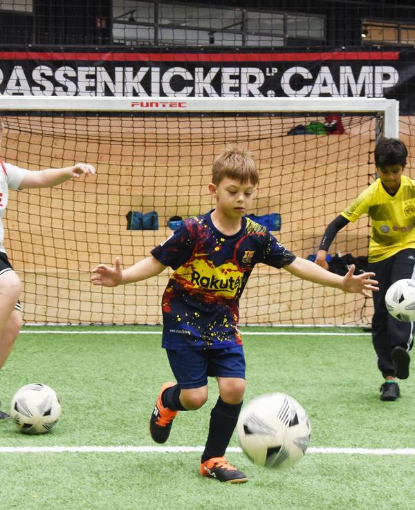 Drei Jungen (v.l Mats, Ilyas und Tom) dribbeln beim „Strassenkicker.Camp” in Köln-Mülheim auf einem Kunstrasenplatz.