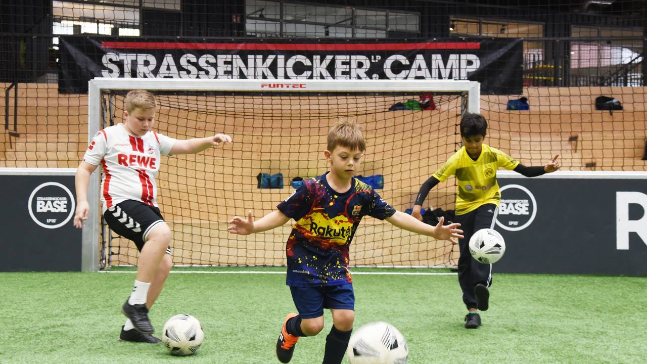 Drei Jungen (v.l Mats, Ilyas und Tom) dribbeln beim „Strassenkicker.Camp” in Köln-Mülheim auf einem Kunstrasenplatz.