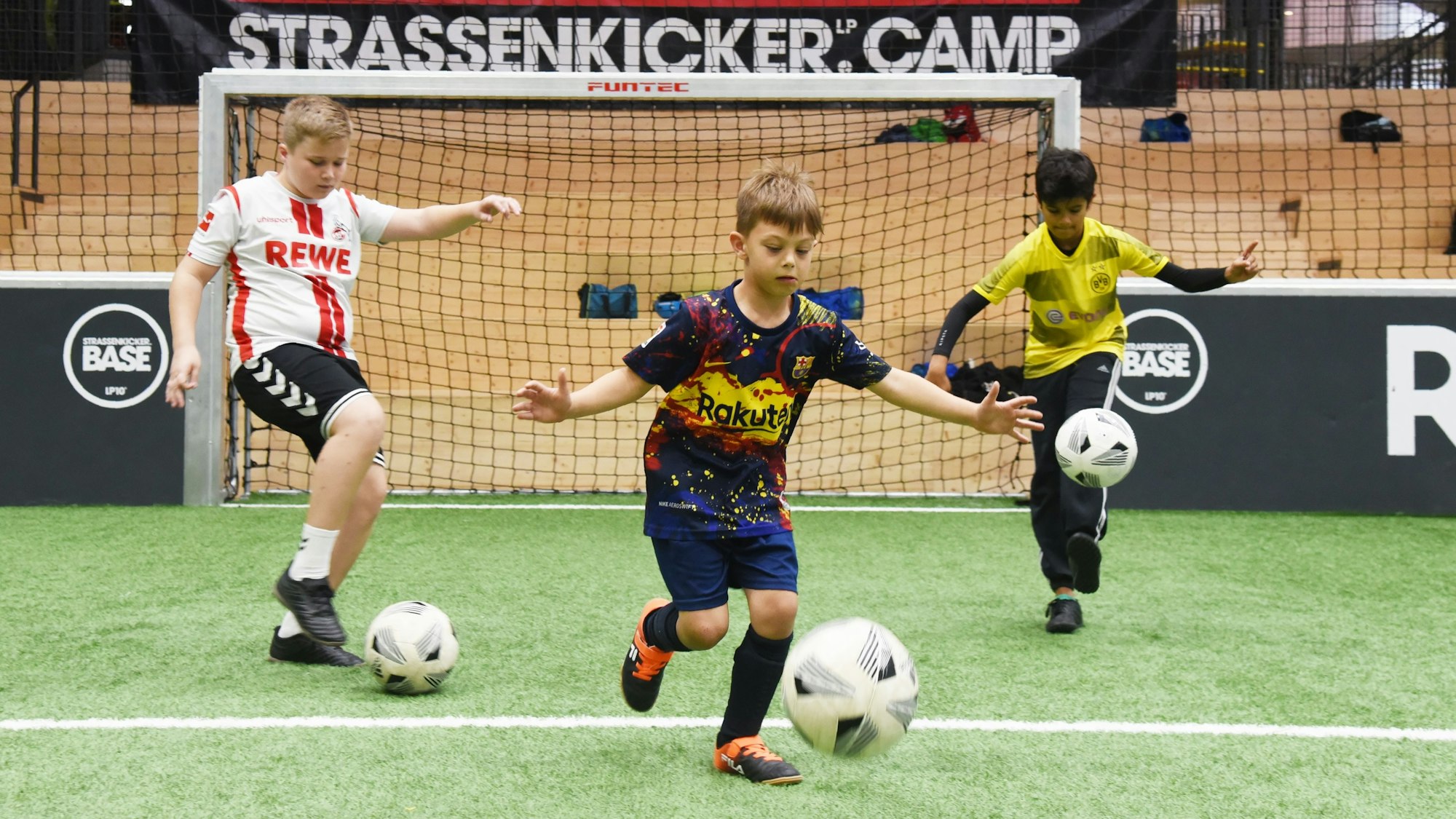 Drei Jungen (v.l Mats, Ilyas und Tom) dribbeln beim „Strassenkicker.Camp” in Köln-Mülheim auf einem Kunstrasenplatz.