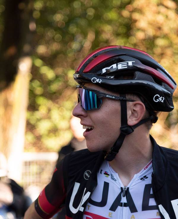 Tadej Pogacar lächelt nach einem langen Rennen. Auf seinem Kopf trägt er einen Helm. Außerdem trägt er eine Sonnenbrille.