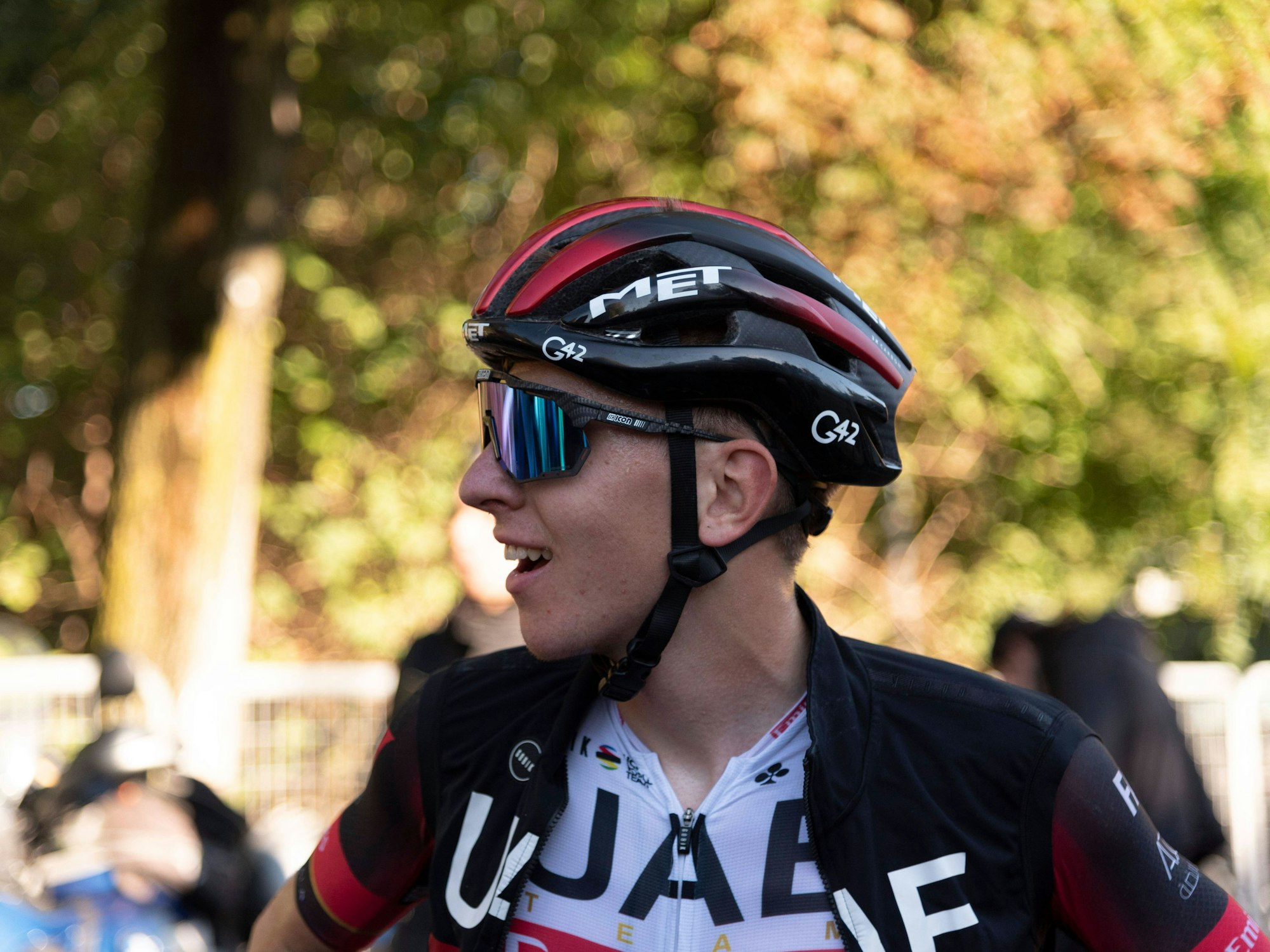 Tadej Pogacar lächelt nach einem langen Rennen. Auf seinem Kopf trägt er einen Helm. Außerdem trägt er eine Sonnenbrille.
