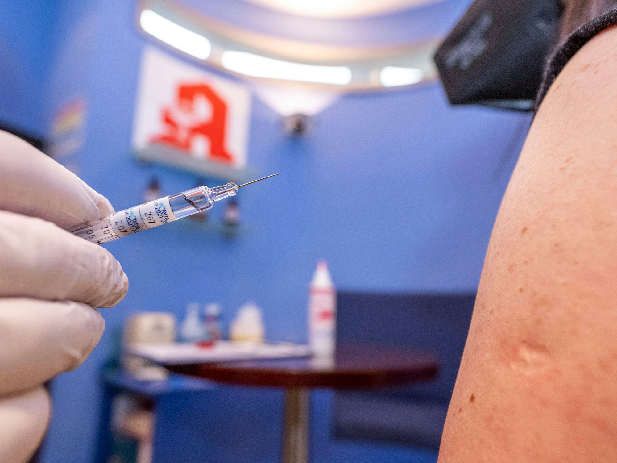 Ein Apotheker hält nah an dem Arm einer Kundin seiner Apotheke eine Spritze mit Grippeschutzimpfstoff.