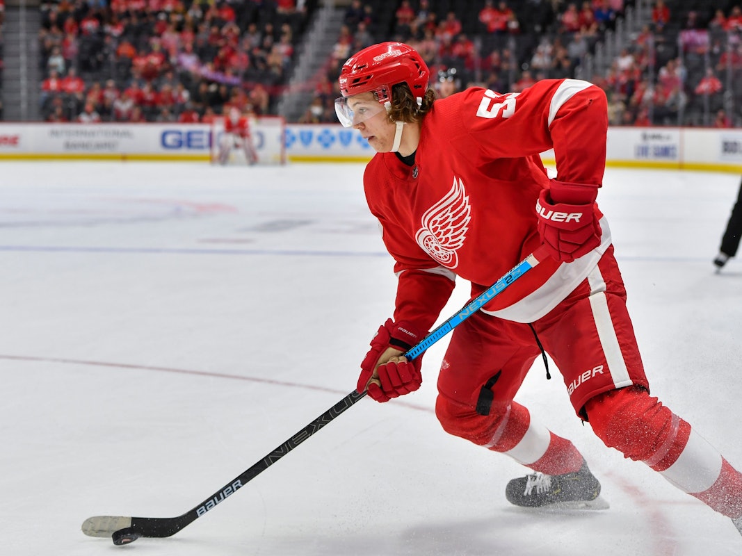 Moritz Seider läuft mit dem roten Trikot der Detroit Red Wings über das Eis und führt den Puck eng am Schläger.