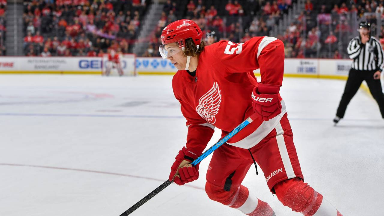 Moritz Seider läuft mit dem roten Trikot der Detroit Red Wings über das Eis und führt den Puck eng am Schläger.