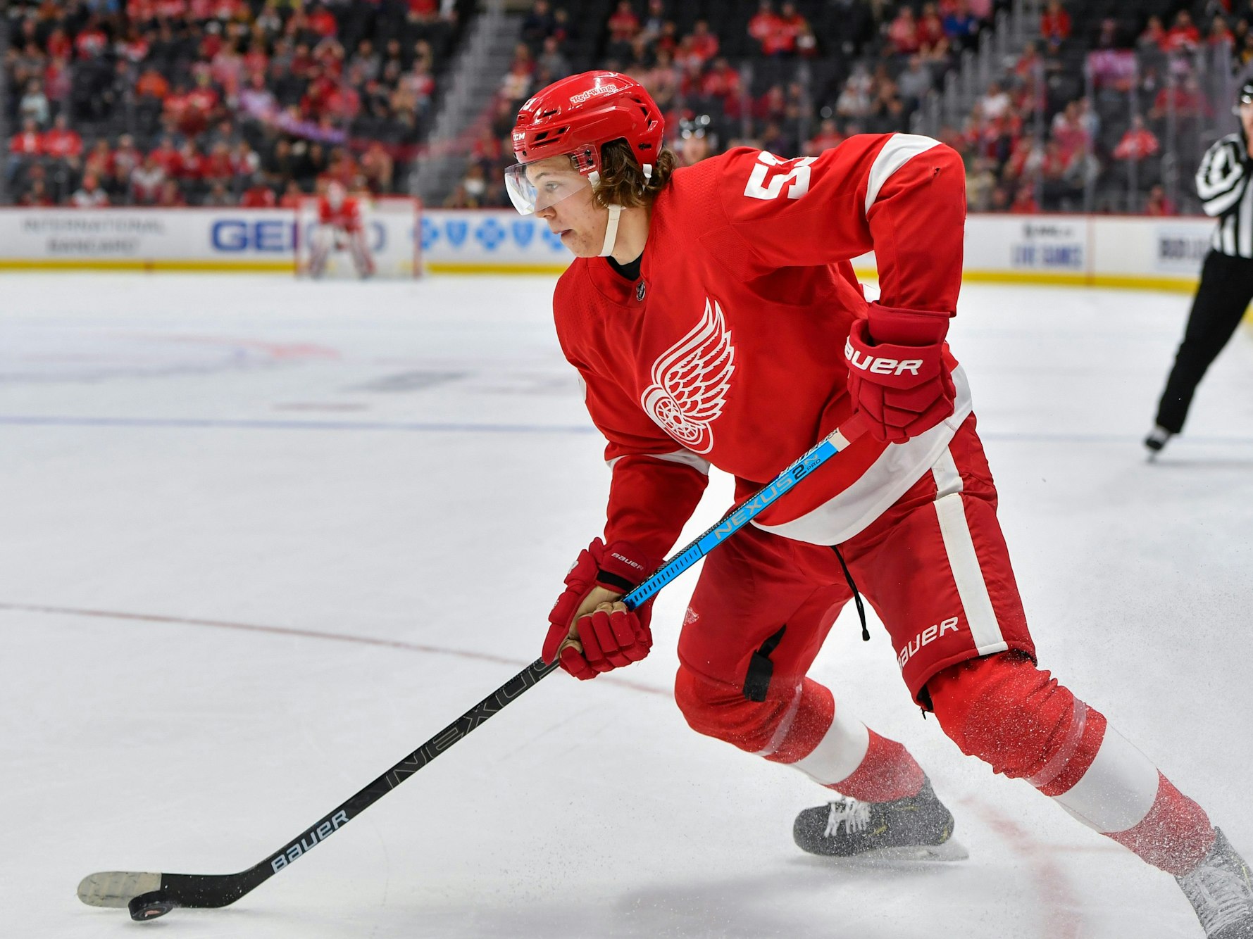 Moritz Seider läuft mit dem roten Trikot der Detroit Red Wings über das Eis und führt den Puck eng am Schläger.