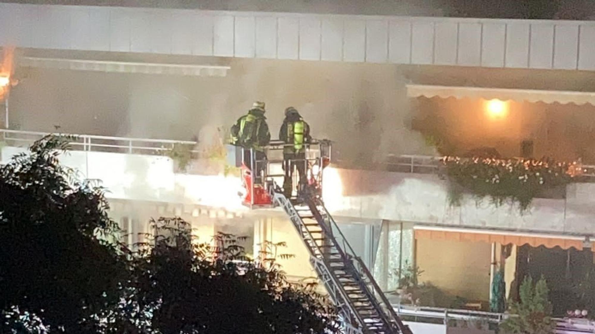 Zwei Wehrmänner stehen auf einer Drehleiter, während aus dem Haus dichter Rauch quillt.