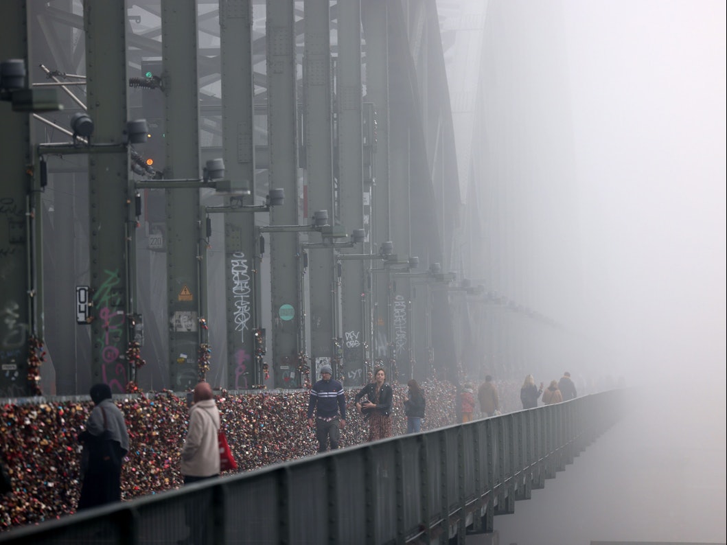 Spaziergänger gehen im Nebel über die Hohenzollernbrücke.