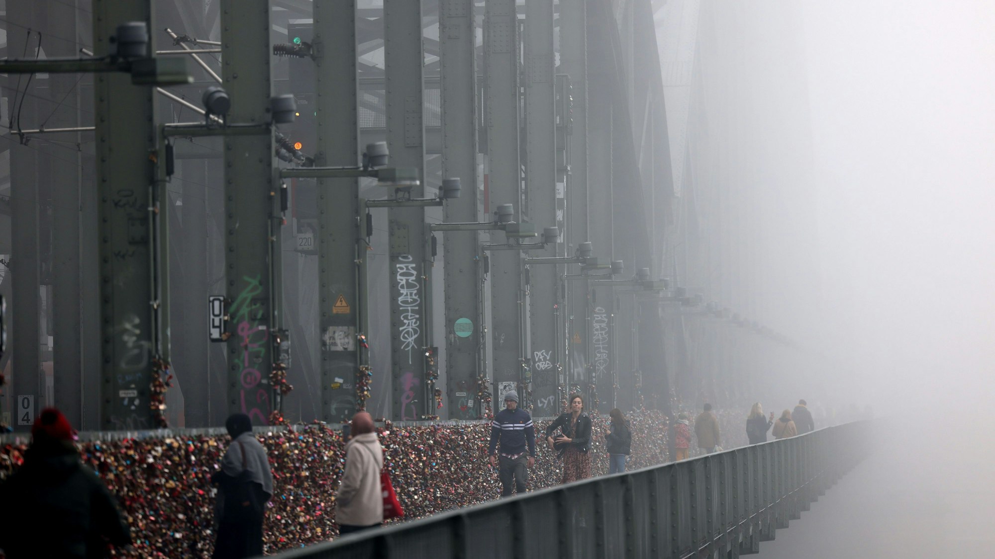 Spaziergänger gehen im Nebel über die Hohenzollernbrücke.