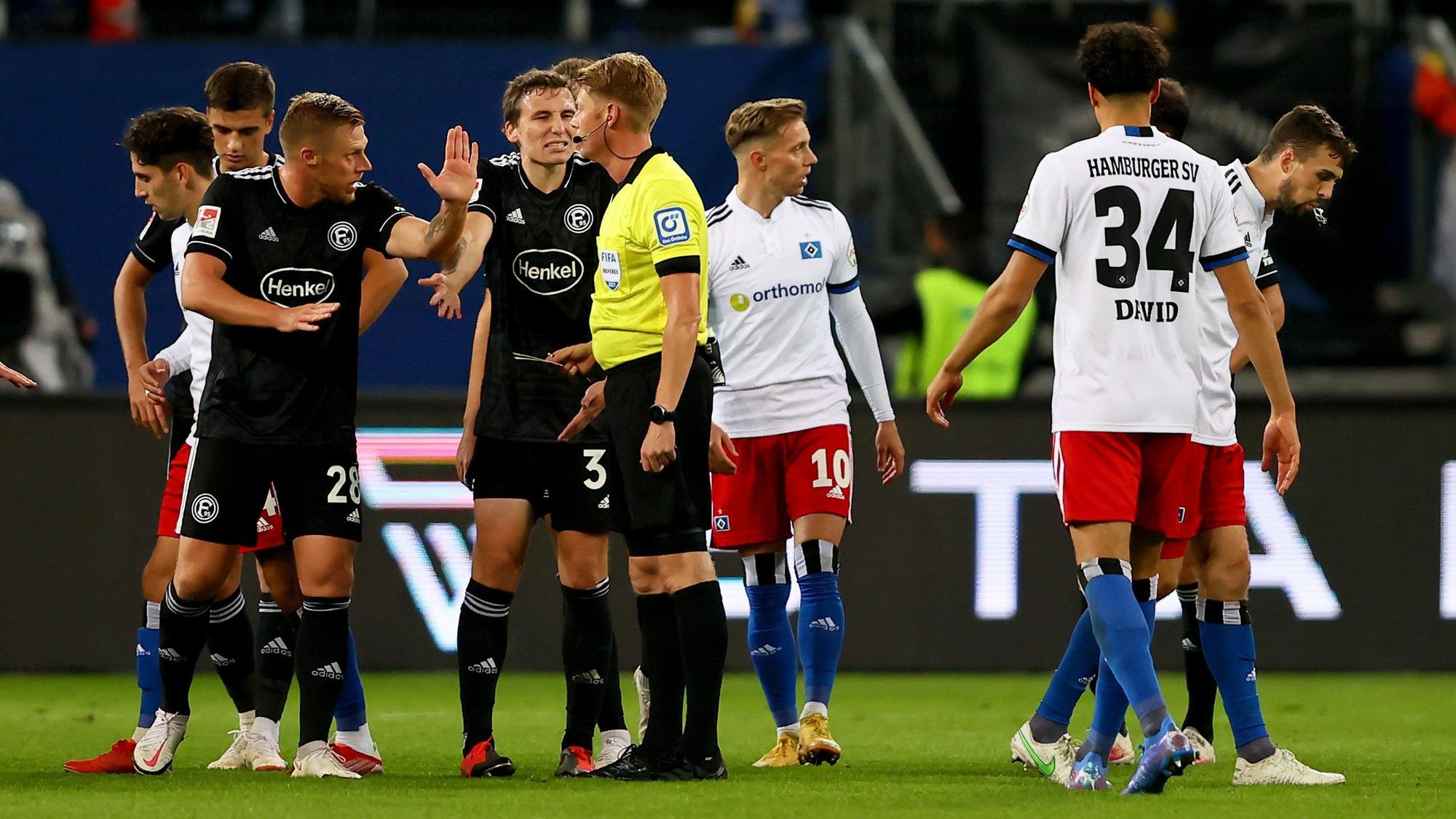 Die Spieler von Fortuna Düsseldorf und dem HSV diskutieren mit Schiedsrichter Christian Dingert.