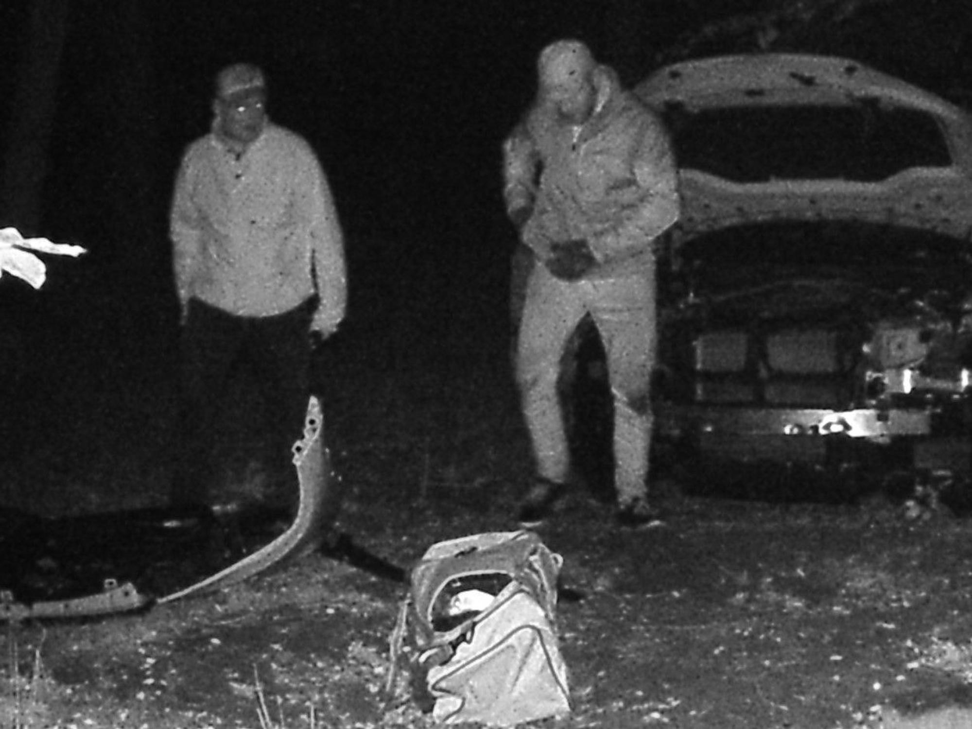 Zwei Männer stehen vor dem geklauten BMW, vor ihnen liegt die bereits abmontierte Stoßstange.