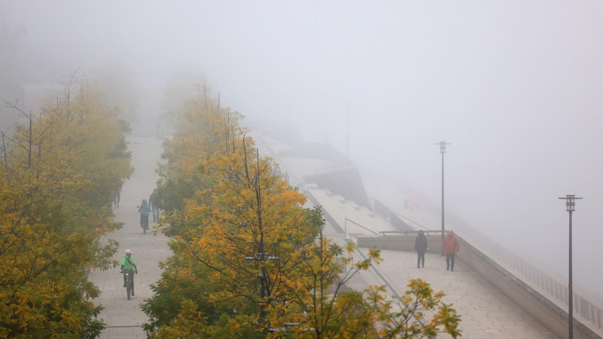 Radfahrer und Spaziergänger sind im Nebel am Kölner Rheinufer unterwegs.