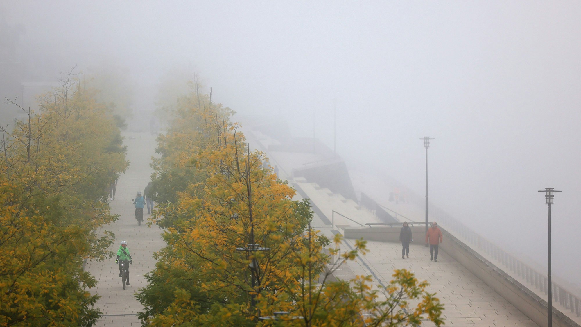 Radfahrer und Spaziergänger sind im Nebel am Kölner Rheinufer unterwegs.