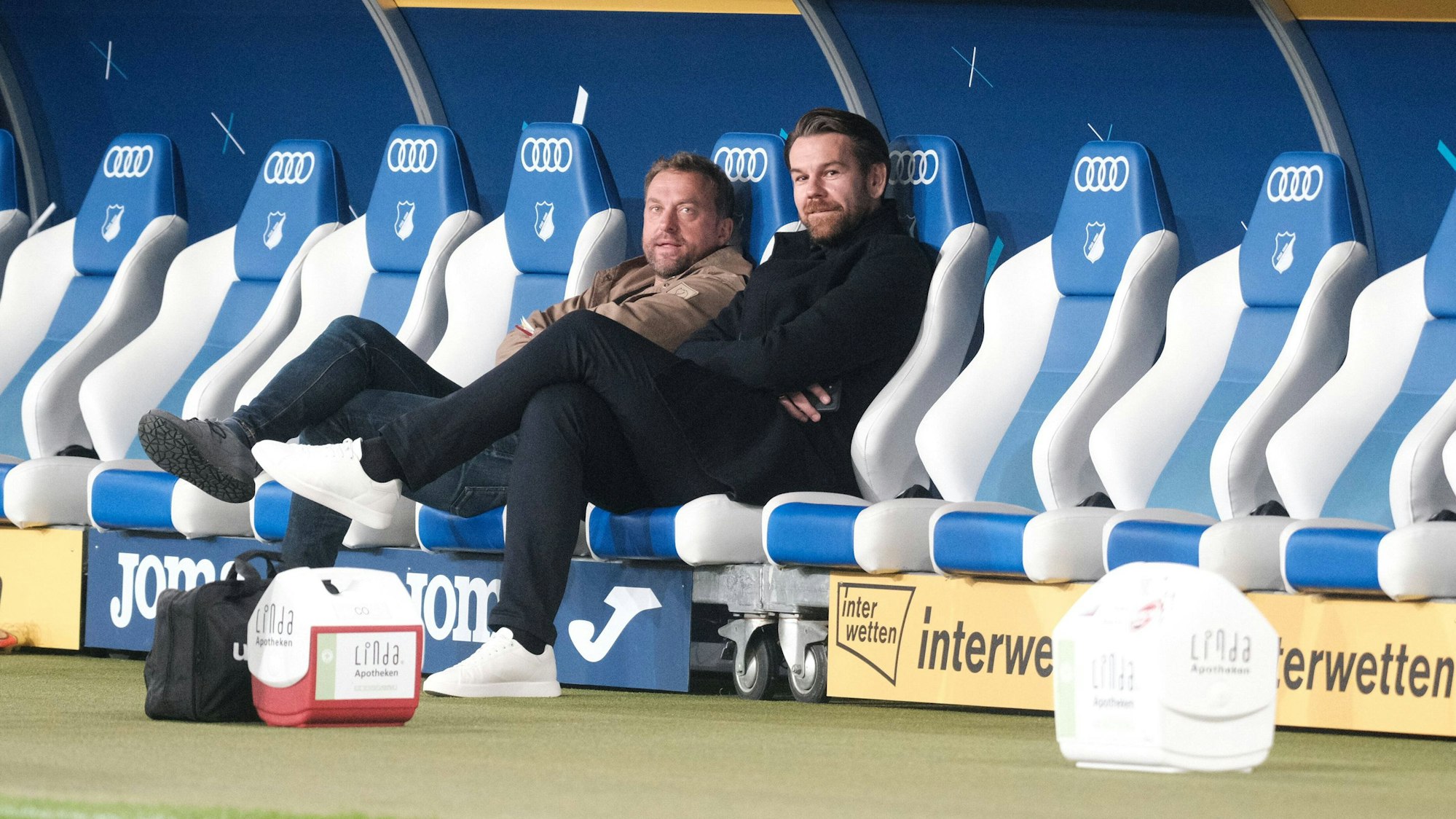Thomas Kessler und Jörg Jakobs sitzen bei der Partie TSG Hoffenheim gegen 1. FC Köln auf der Bank.