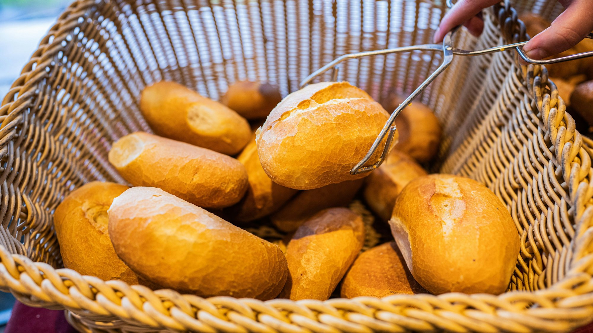 Eine Verkäuferin nimmt ein Brötchen mit einer Zange aus einem Brötchenkorb. Werden Brötchen bald teurer? Mit ein Grund: die stark gestiegenen Getreidepreise.