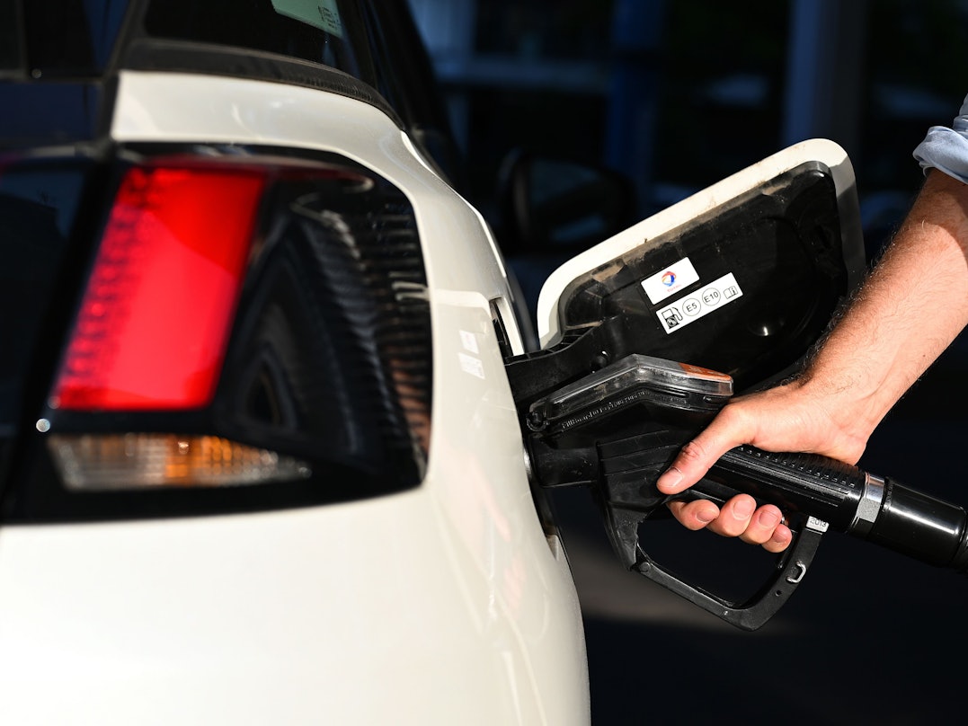 Ein Mann betankt sein weißes Auto, nur seine Hand mit der Spritzpistole ist zu sehen.