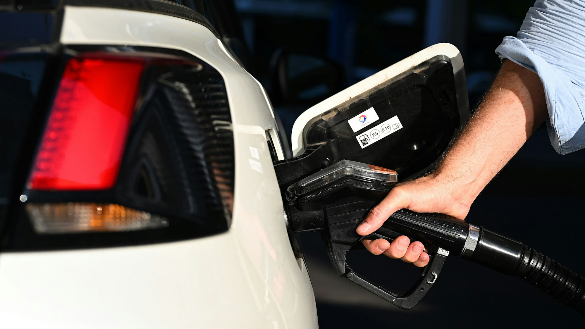 Ein Mann betankt sein weißes Auto, nur seine Hand mit der Spritzpistole ist zu sehen.