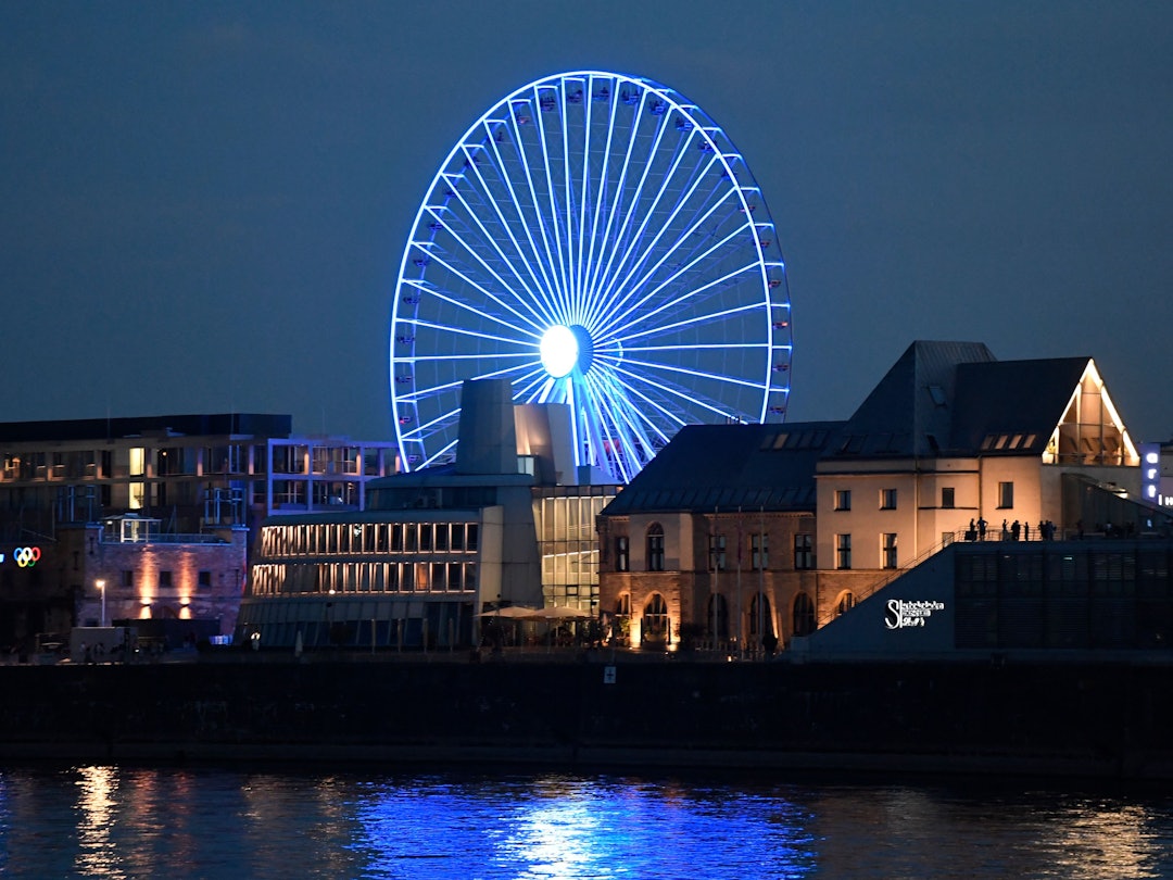 Das Riesenrad am Rheinufer strahlt bei Nacht.