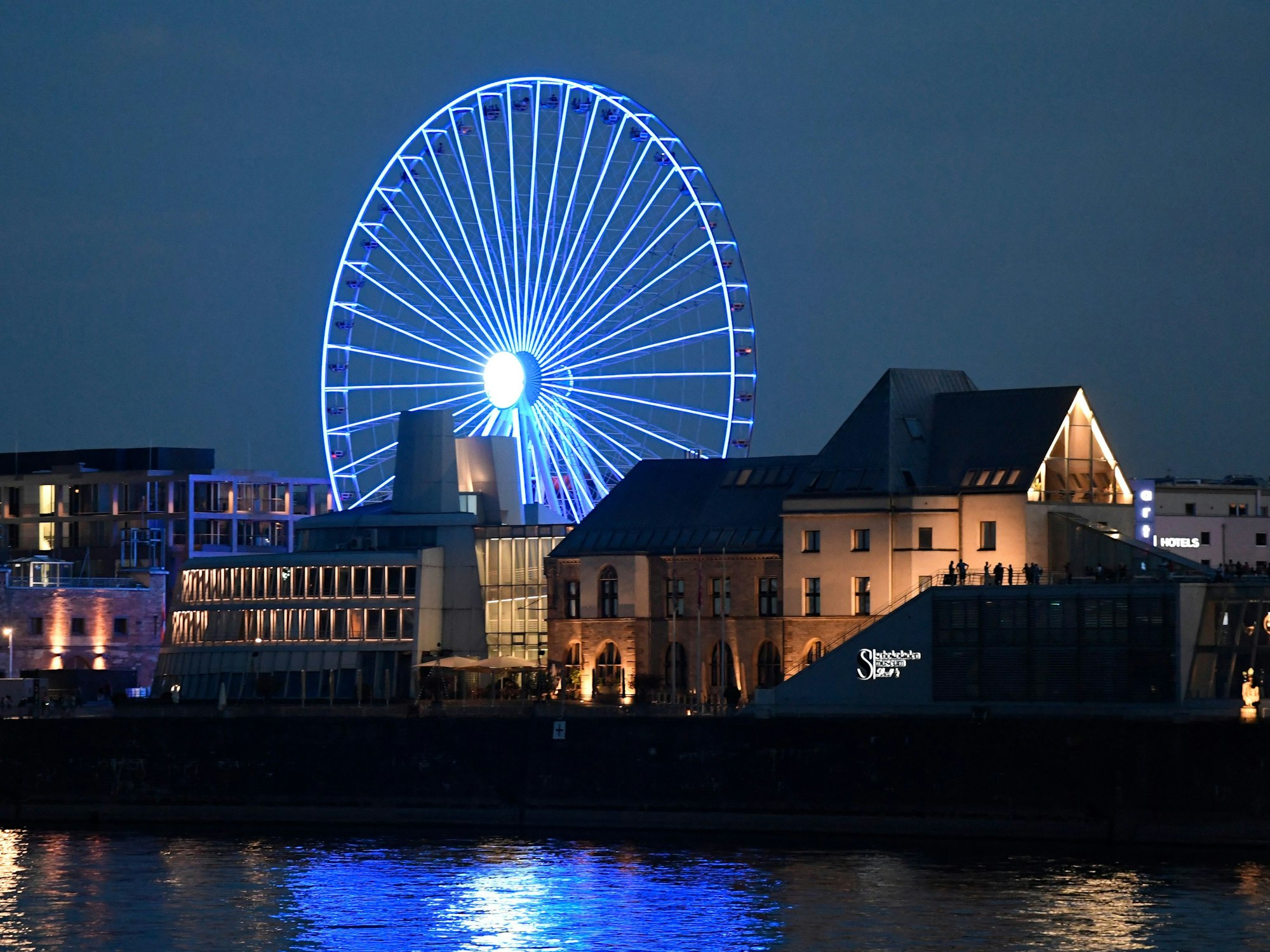 Das Riesenrad am Rheinufer strahlt bei Nacht.