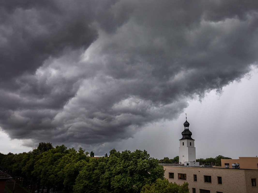 Dunkle Wolken ziehen am 4. Juli 2021 kurz vor einem Gewitter mit Starkregen über den Kölner Ortsteil Sülz. Der Kirchturm rechts gehört zur Kirche „Zur heiligen Familie“.