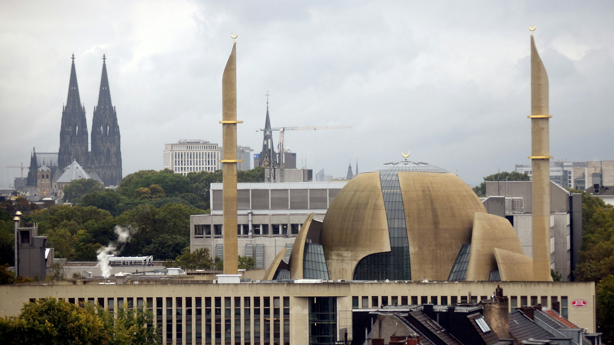 Im Vordergrund ragen zwei Minarette der Großmoschee in den Himmel, im Hintergrund steht der Kölner Dom.