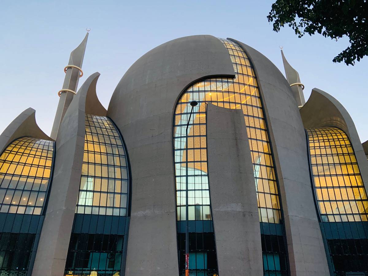 Die Zentralmoschee in Köln-Ehrenfeld leuchtet in der Abenddämmerung von innen.