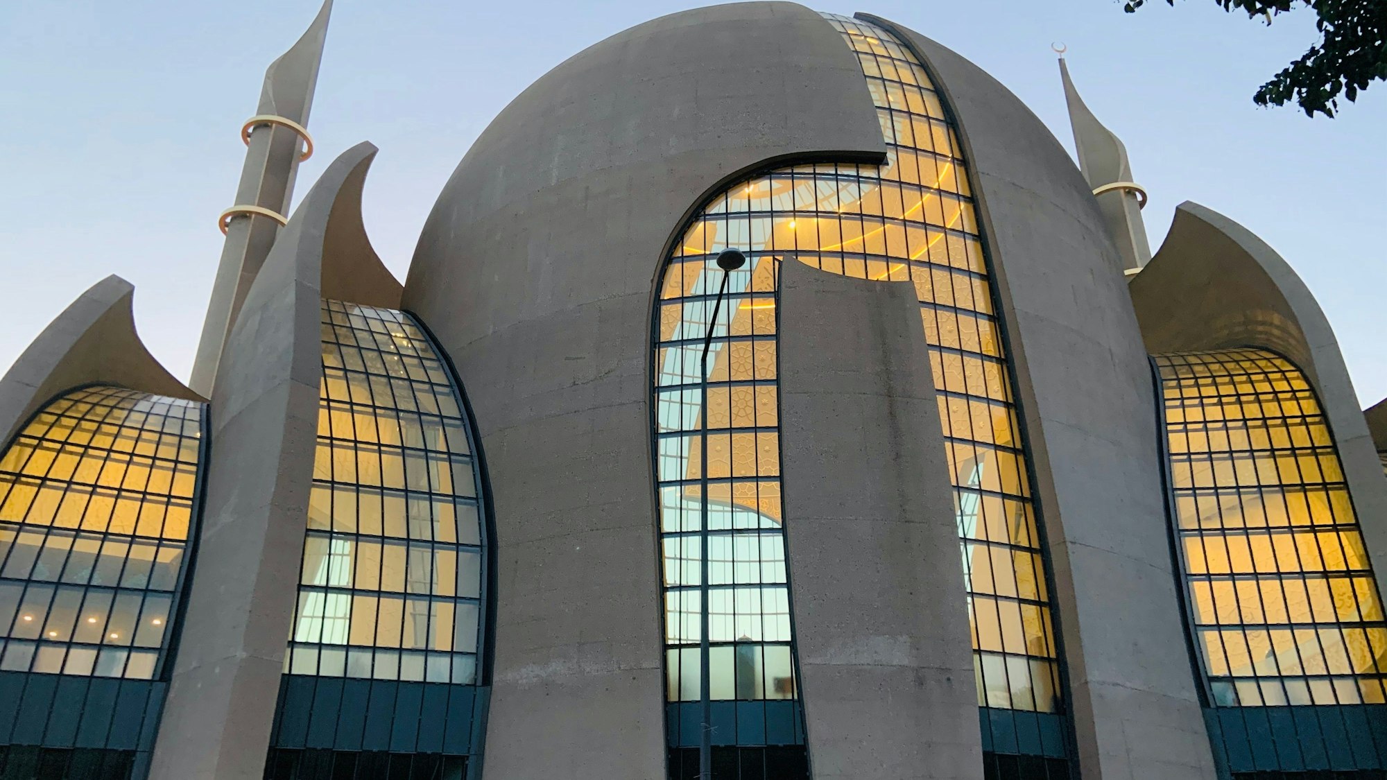 Die Zentralmoschee in Köln-Ehrenfeld leuchtet in der Abenddämmerung von innen.