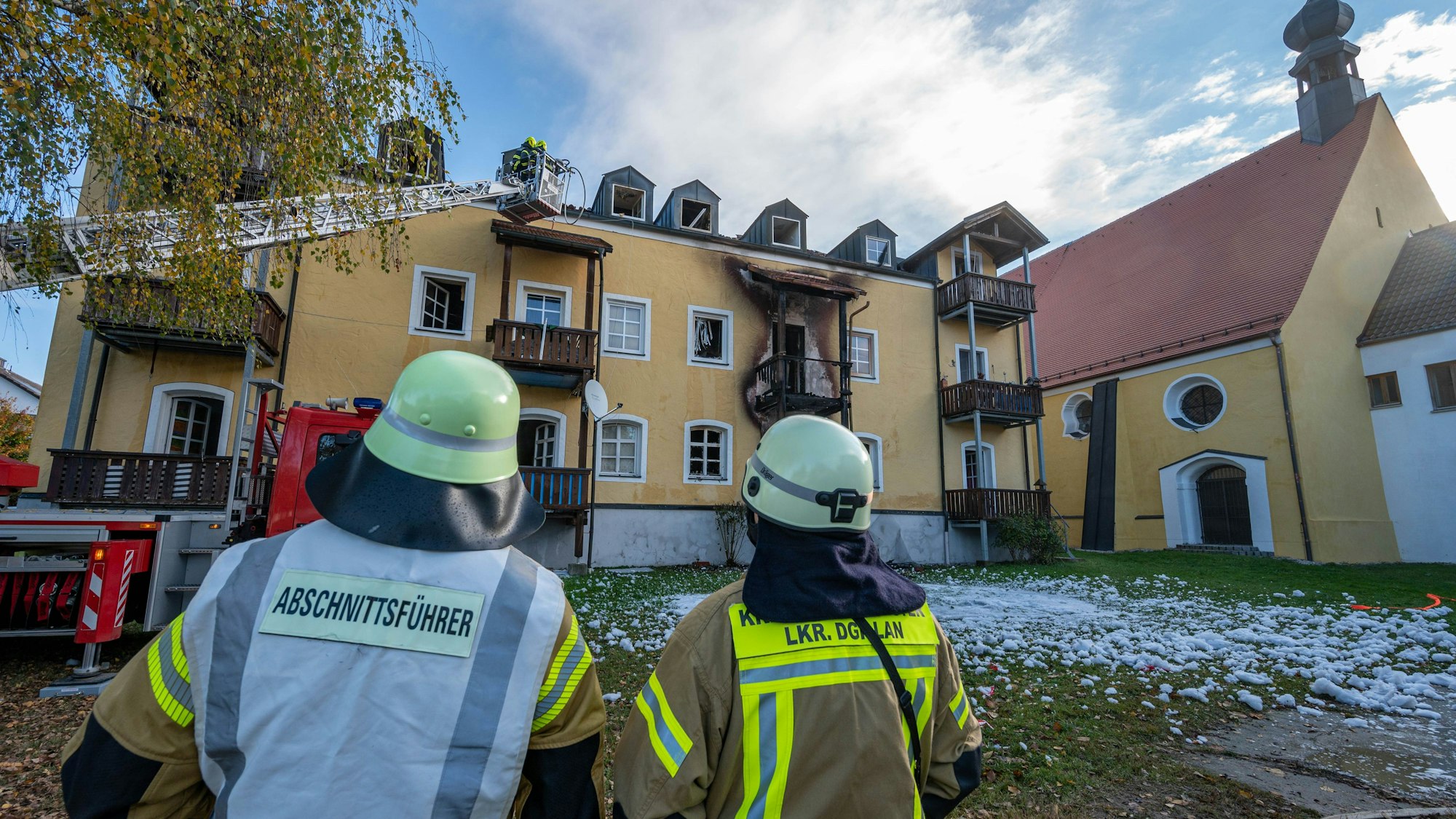 Feuerwehrleute stehen vor einem ausgebrannten Mehrfamilienhaus. Drei Frauen und ein frühgeborenes Baby sind in dem Haus in Reisbach bei einem Brand ums Leben gekommen.