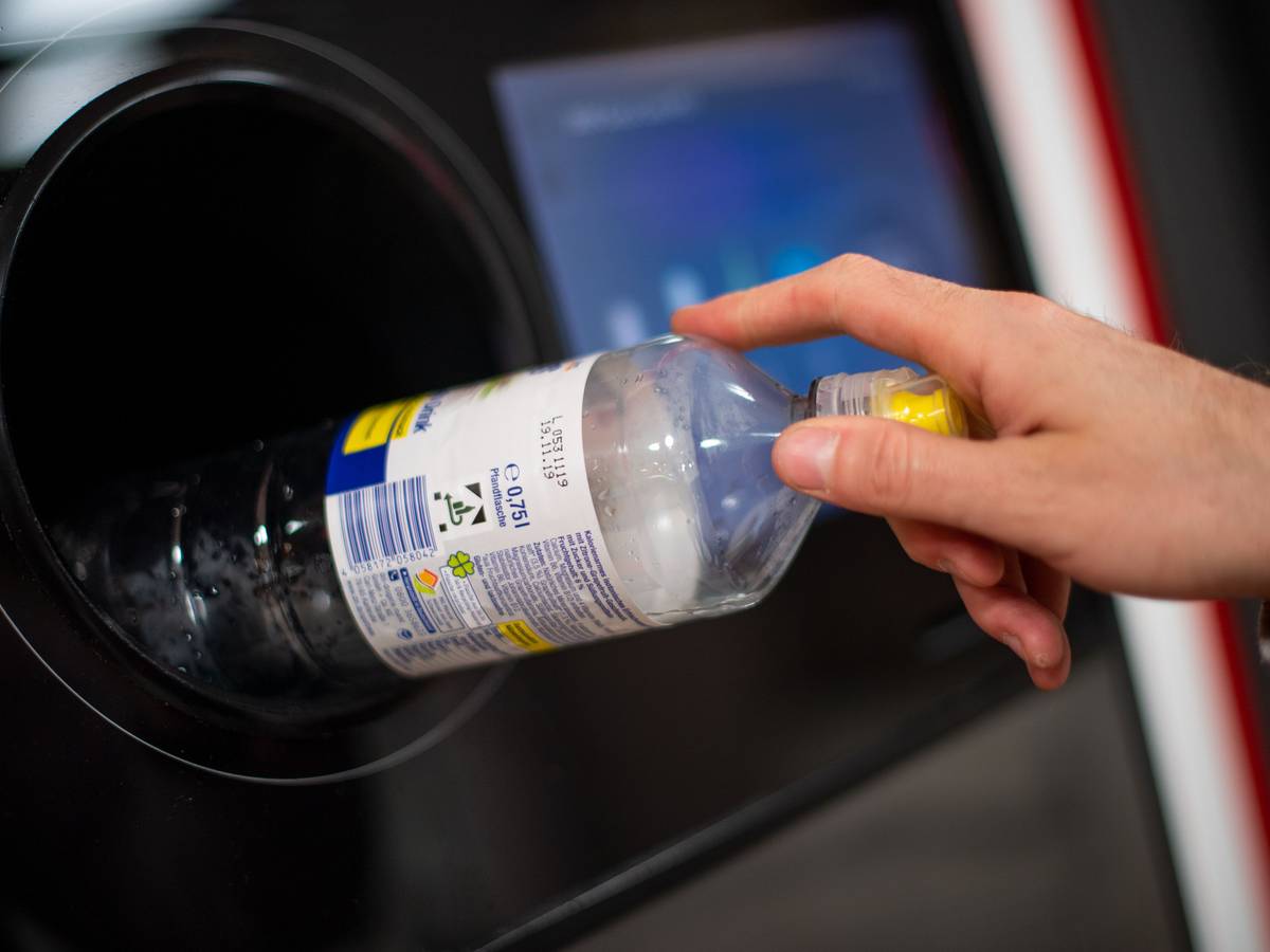 Ein Mann steckt eine Pfandflasche in einen Pfandflaschenautomaten in einem Supermarkt.