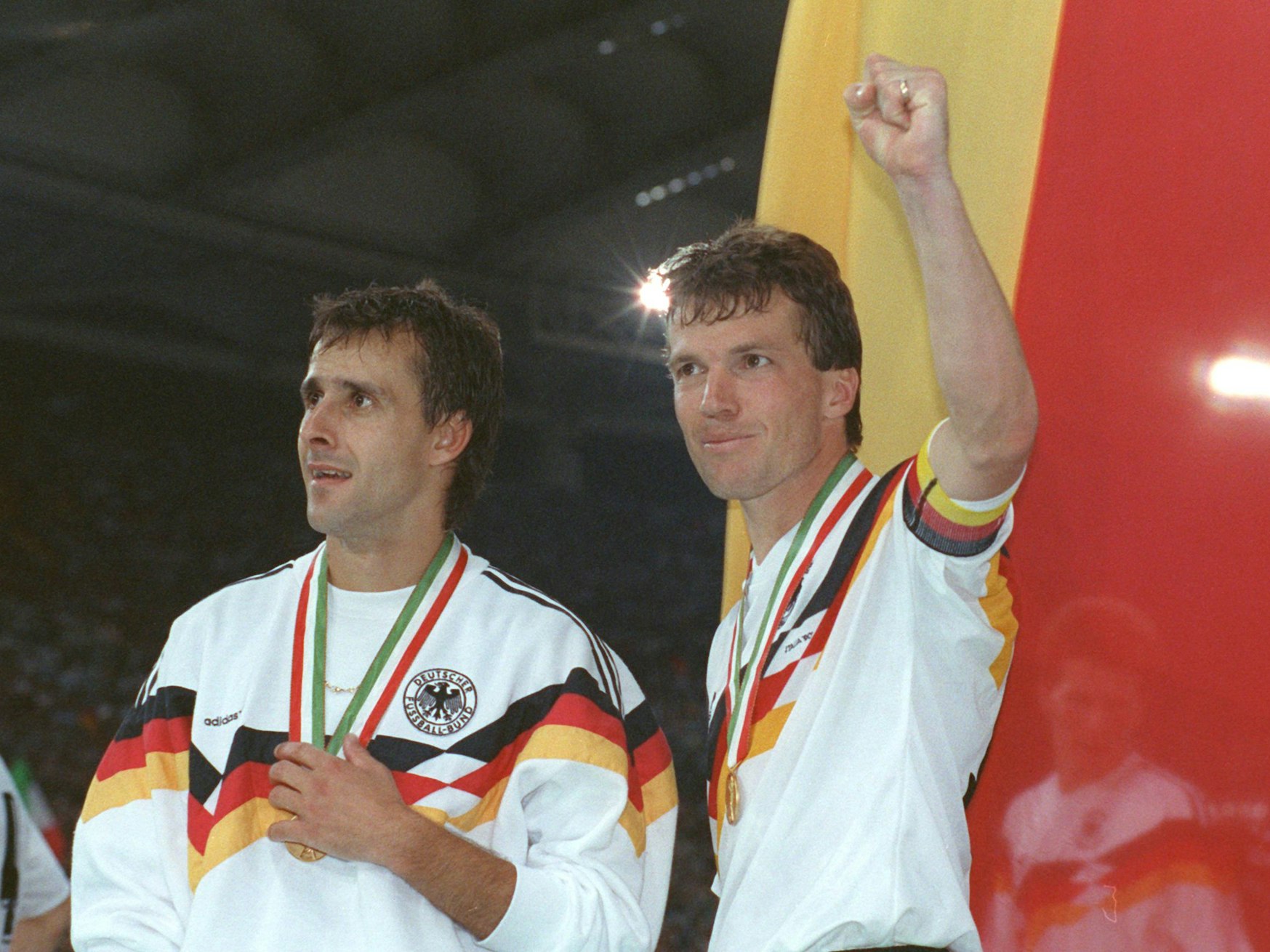 Der deutsche Mittelfeldspieler und Kapitän Lothar Matthäus (r.) und sein Mitstreiter Pierre Littbarski (l.) bejubeln vor der deutschen Fahne den WM-Titel.