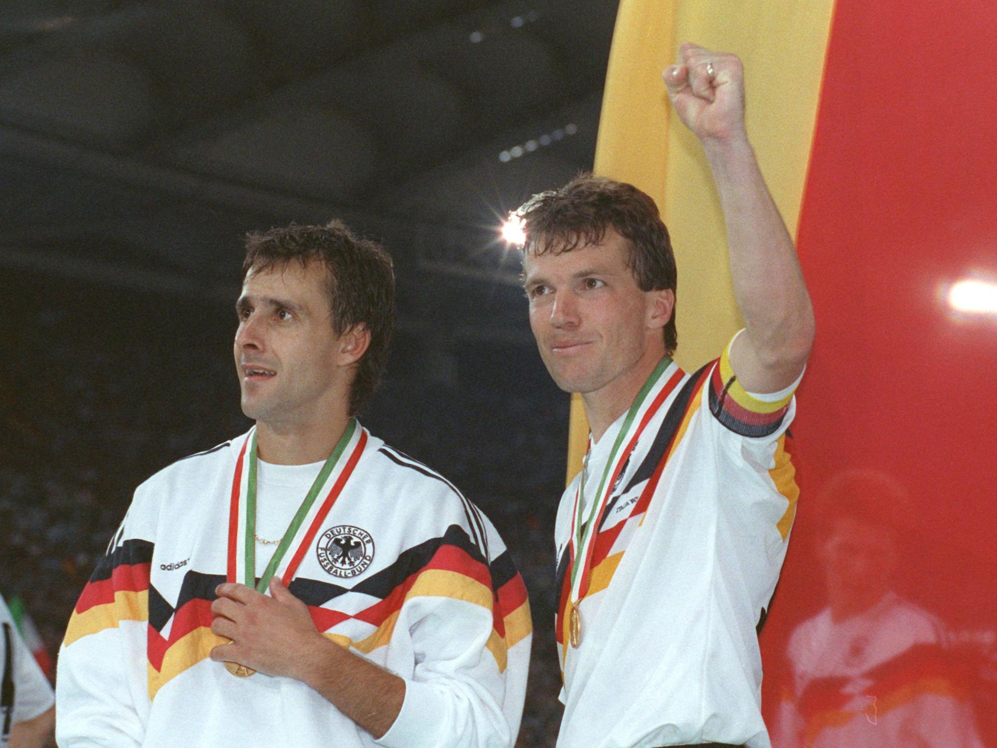 Der deutsche Mittelfeldspieler und Kapitän Lothar Matthäus (r.) und sein Mitstreiter Pierre Littbarski (l.) bejubeln vor der deutschen Fahne den WM-Titel.