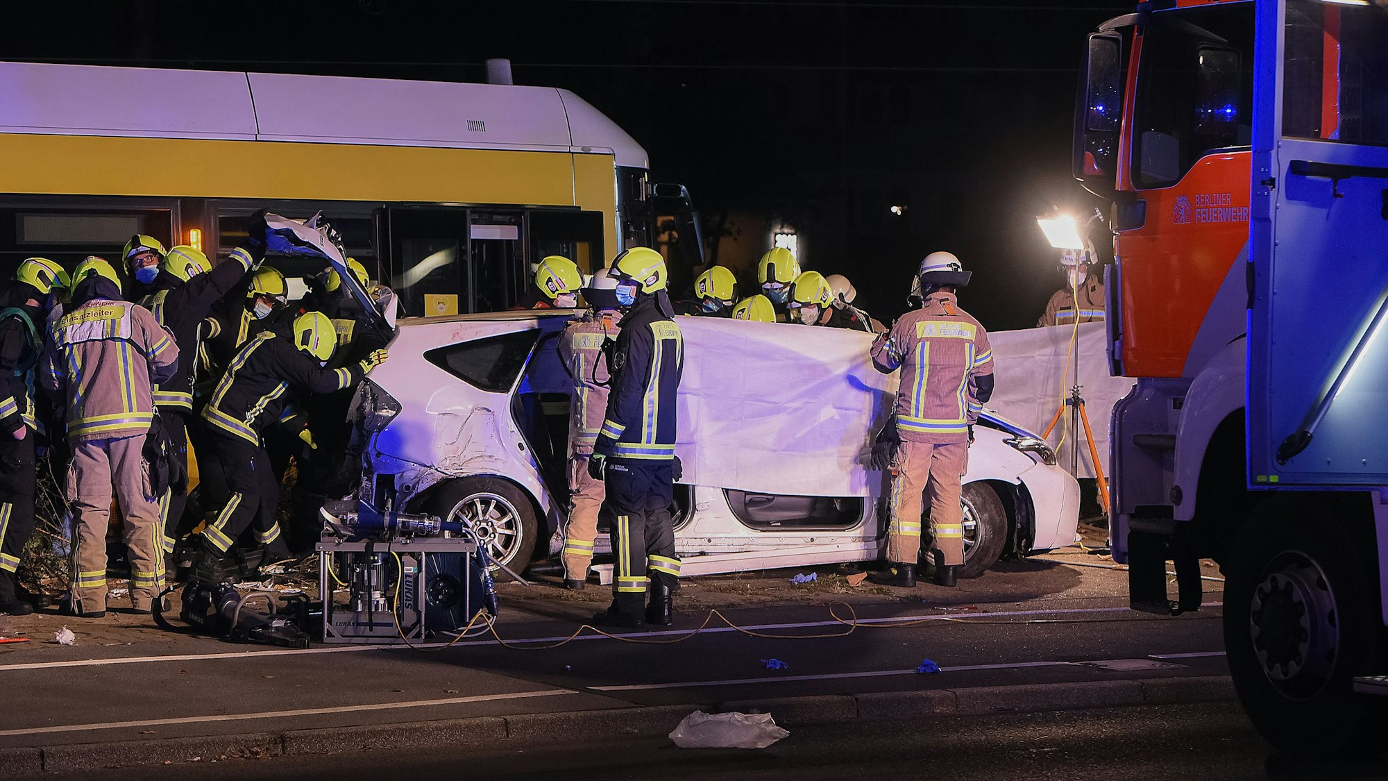 Einsatzkräfte halten am frühen Sonntagmorgen neben einer Straßenbahn an der Liebenwalder Straße / Landsberger Allee in Lichtenberg ein Tuch als Sichtschutz bei der Bergung einer Leiche.