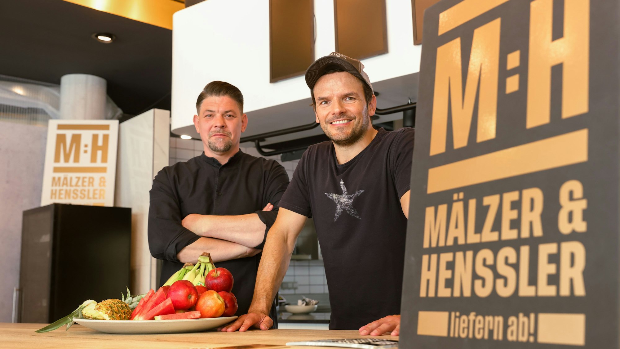 Tim Mälzer und Steffen Henssler stehen im Studio der neuen Kochshow „Mälzer und Henssler liefern ab!“ bei Vox