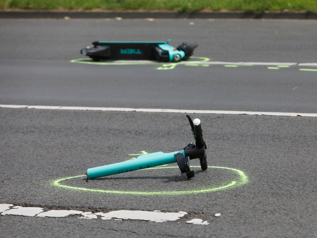 Ein in zwei Teile gerissener E-Scooter liegt auf einer Straße. Die Polizei hat beide Stelle mit Farbe markiert.